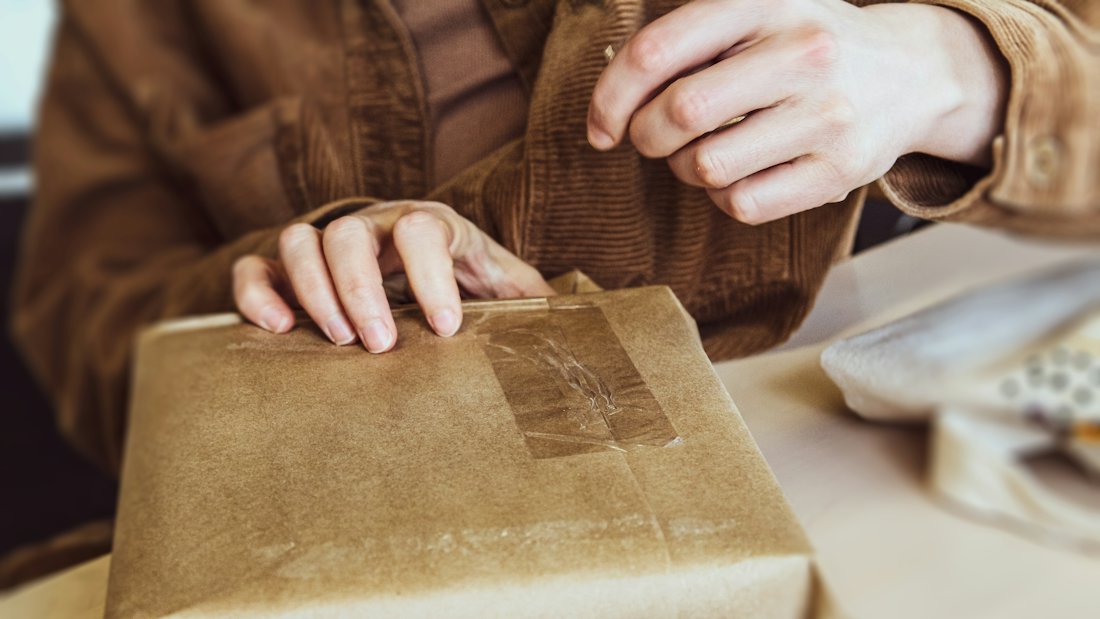 Mani che chiudono con il nastro adesivo un pacco in carta da spedire